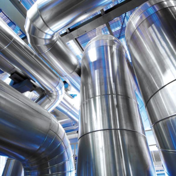 Nahaufnahme mehrerer vertikaler und horizontaler Rohrleitungen mit glänzender Aluminium-Blechverkleidung in einer Industrieanlage