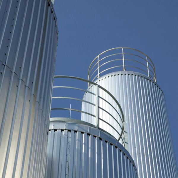 Froschperspektive auf mehrere silberne Silos vor einem blauen Himmel
